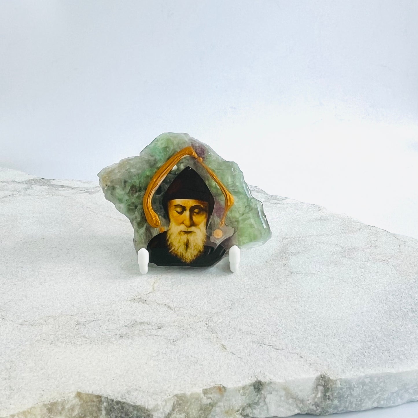Saint Charbel Maronite Icon is carefully handcrafted on Flourite, covered with a clear hypoxy resin.  Comes with a white stand.